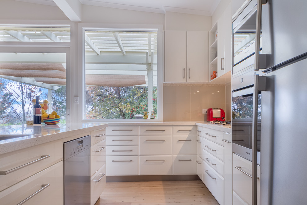 Inspiration for a large contemporary l-shaped light wood floor open concept kitchen remodel in Sydney with an undermount sink, white cabinets, solid surface countertops, beige backsplash, ceramic backsplash, stainless steel appliances and an island