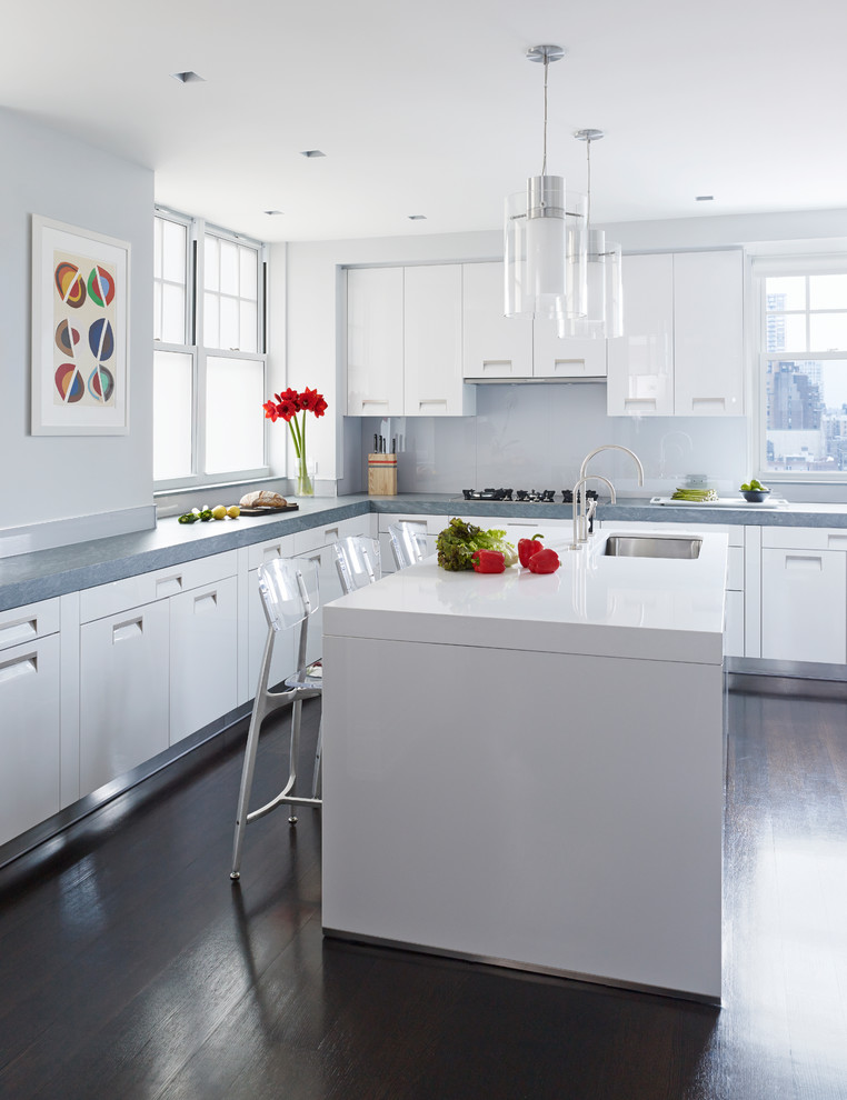 ニューヨークにあるコンテンポラリースタイルのおしゃれなキッチン (アンダーカウンターシンク、フラットパネル扉のキャビネット、白いキャビネット、白いキッチンパネル、ガラス板のキッチンパネル、濃色無垢フローリング、茶色い床、グレーのキッチンカウンター) の写真