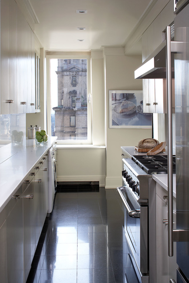 Modelo de cocina estrecha actual con armarios con paneles lisos, puertas de armario blancas y electrodomésticos de acero inoxidable