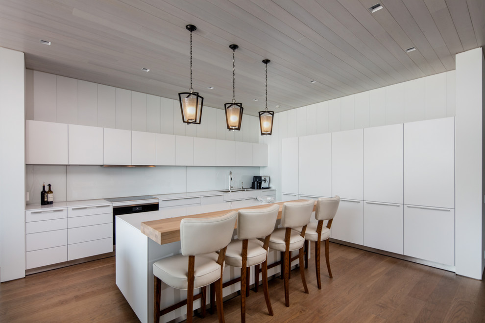 Example of a mid-sized beach style medium tone wood floor kitchen design in Toronto with flat-panel cabinets, white cabinets, white backsplash, an island, white countertops and a double-bowl sink