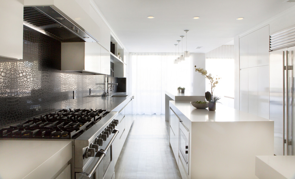 Example of a large minimalist eat-in kitchen design in Los Angeles with an undermount sink, flat-panel cabinets, white cabinets, quartz countertops, black backsplash, stone slab backsplash and stainless steel appliances
