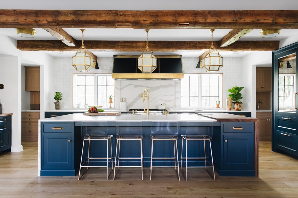 Photo of a classic kitchen in Grand Rapids with shaker cabinets, blue cabinets, white splashback, stone slab splashback, medium hardwood flooring, an island and white worktops.