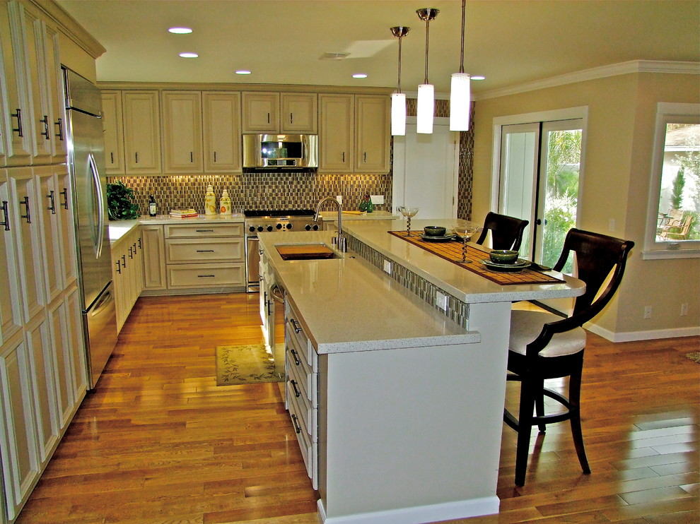 Example of a mid-sized classic l-shaped medium tone wood floor and brown floor open concept kitchen design in Los Angeles with a single-bowl sink, raised-panel cabinets, beige cabinets, quartzite countertops, multicolored backsplash, stainless steel appliances, an island and glass sheet backsplash