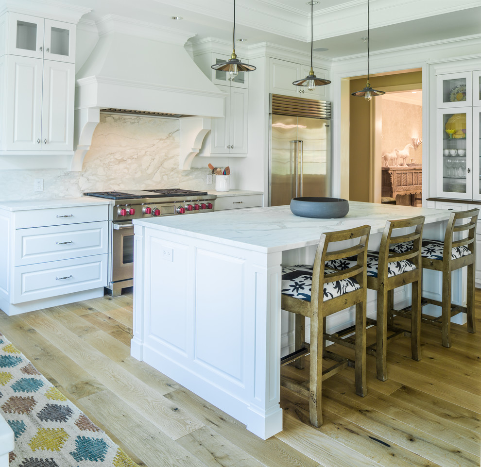Klassische Küche in L-Form mit profilierten Schrankfronten, weißen Schränken, Küchenrückwand in Weiß, Rückwand aus Stein, Küchengeräten aus Edelstahl, hellem Holzboden, Kücheninsel, beigem Boden und weißer Arbeitsplatte in Albuquerque