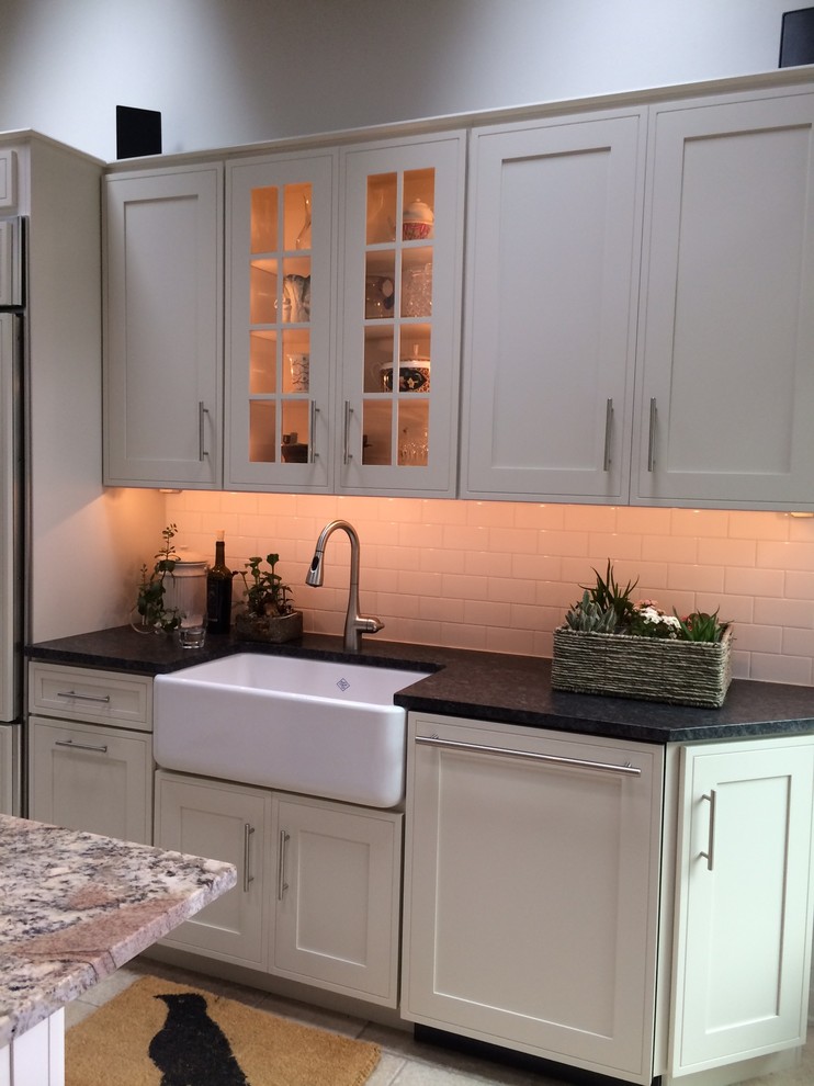 Eat-in kitchen - small transitional galley porcelain tile eat-in kitchen idea in Wilmington with a farmhouse sink, shaker cabinets, white cabinets, granite countertops, white backsplash, subway tile backsplash, an island and stainless steel appliances