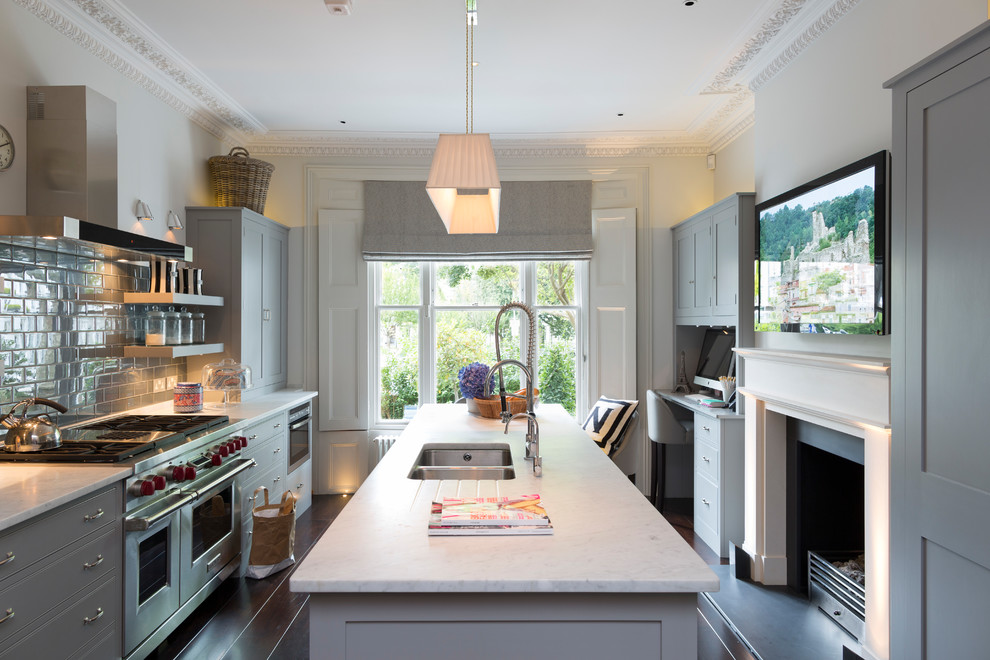 Traditional galley kitchen in London with a double-bowl sink, shaker cabinets, grey cabinets, dark hardwood flooring, an island, brown floors and white worktops.