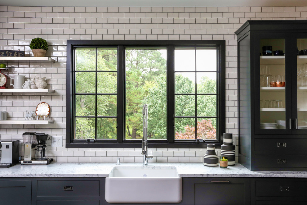 Photo of a large classic u-shaped kitchen/diner in Raleigh with a belfast sink, black cabinets, white splashback, metro tiled splashback, flat-panel cabinets, marble worktops, stainless steel appliances and an island.