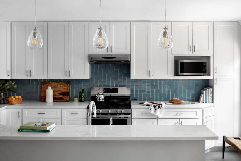 Klassisk inredning av ett vit vitt kök, med en undermonterad diskho, skåp i shakerstil, vita skåp, bänkskiva i kvarts, blått stänkskydd, stänkskydd i glaskakel, rostfria vitvaror, klinkergolv i porslin, en köksö och grått golv