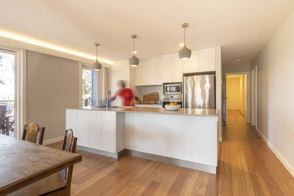 Modelo de cocina contemporánea pequeña abierta con fregadero encastrado, armarios con paneles lisos, puertas de armario blancas, encimera de cuarcita, salpicadero blanco, salpicadero de azulejos de cerámica, electrodomésticos de acero inoxidable, una isla y encimeras grises