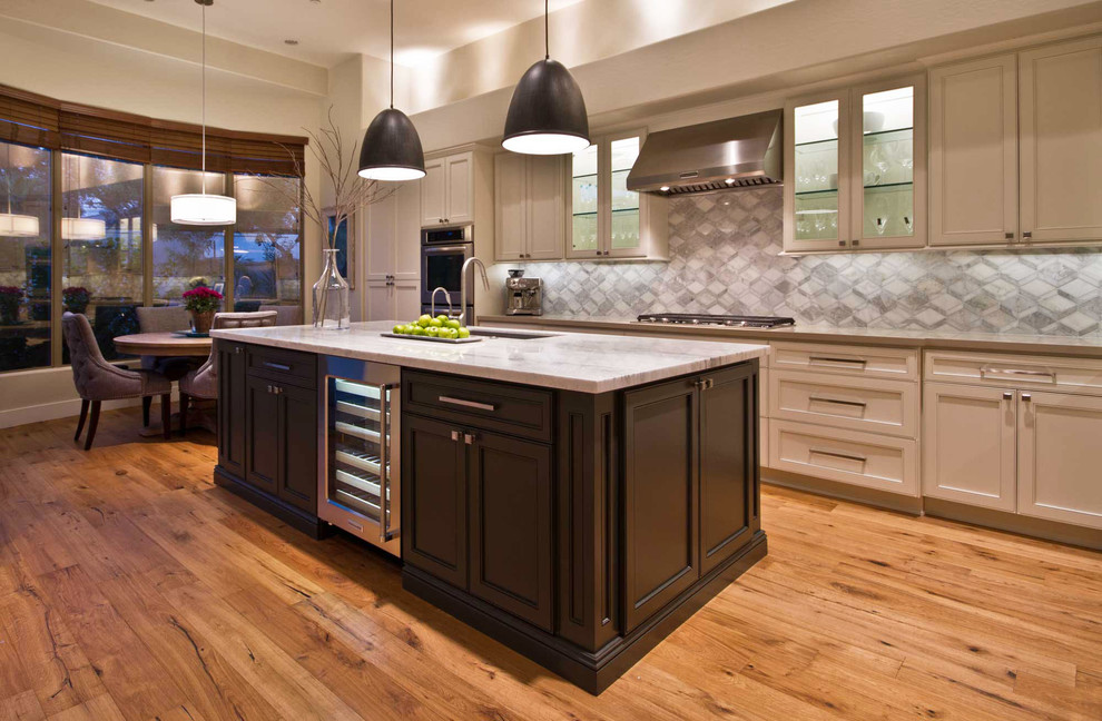 Example of a mid-sized transitional l-shaped medium tone wood floor eat-in kitchen design in Phoenix with a single-bowl sink, recessed-panel cabinets, beige cabinets, quartz countertops, gray backsplash, mosaic tile backsplash, stainless steel appliances and an island