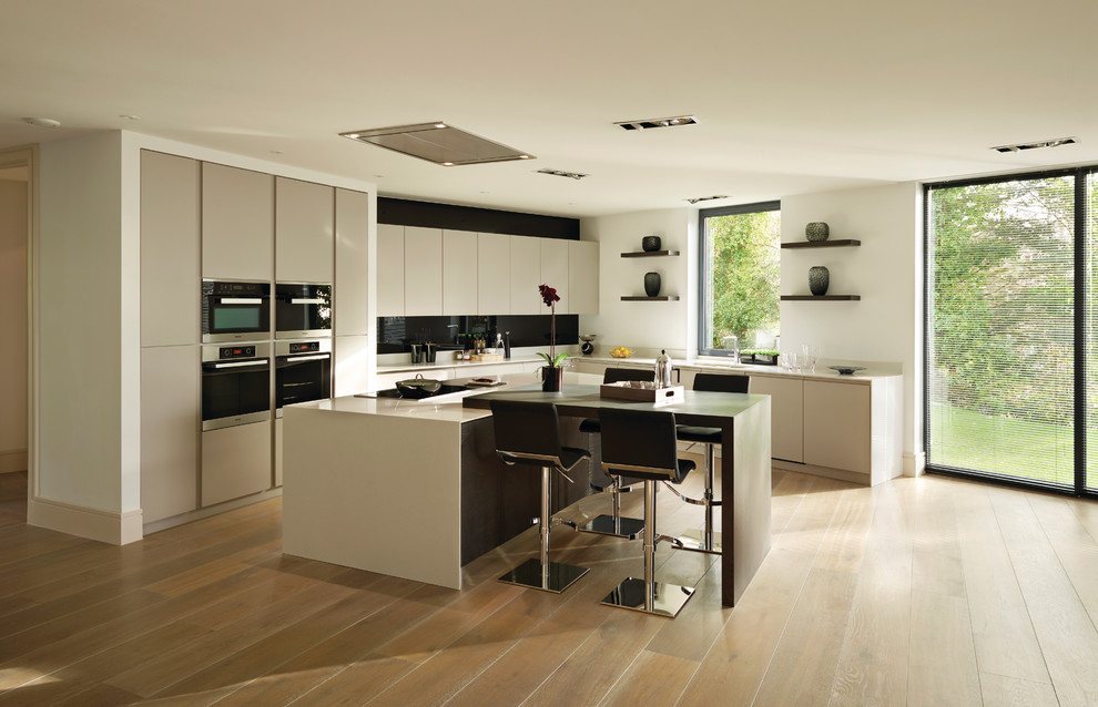 This is an example of a modern l-shaped open plan kitchen in Other with a submerged sink, shaker cabinets, white cabinets, composite countertops, stone slab splashback, stainless steel appliances and an island.