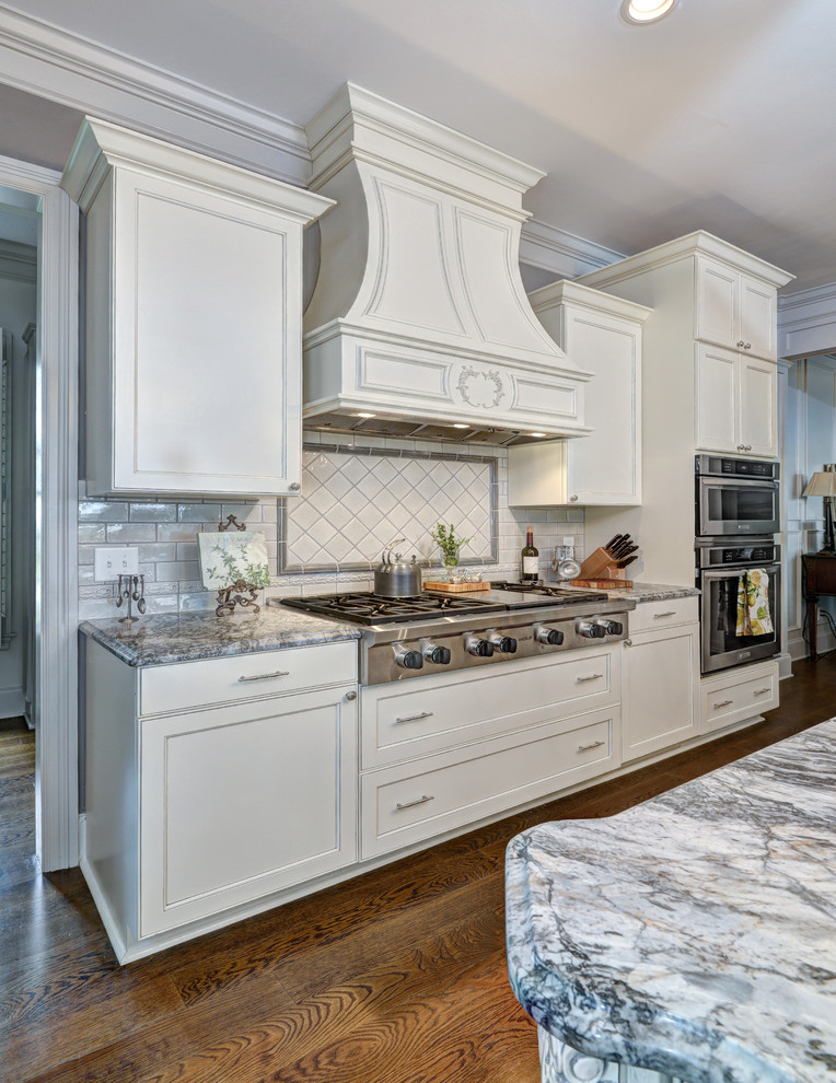 Diseño de cocina comedor clásica extra grande con armarios con paneles empotrados, puertas de armario beige, encimera de granito, salpicadero blanco, salpicadero de azulejos en listel y una isla