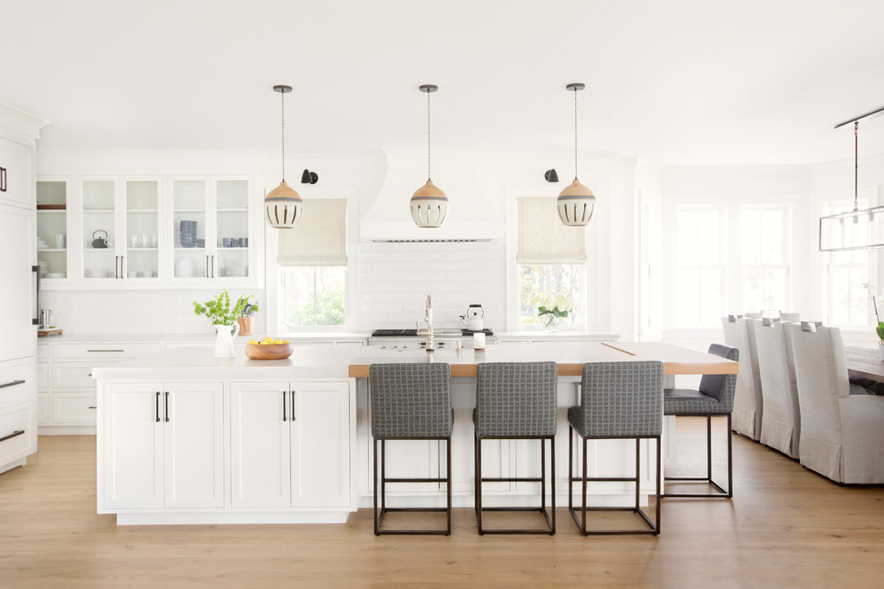 Kitchen - transitional l-shaped light wood floor and beige floor kitchen idea in Charleston with a farmhouse sink, white cabinets, paneled appliances, an island, white countertops, shaker cabinets, white backsplash and subway tile backsplash