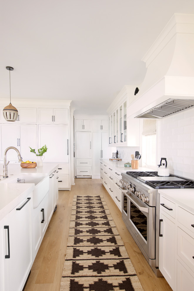 Foto de cocina contemporánea con fregadero sobremueble, puertas de armario blancas, electrodomésticos con paneles, suelo de madera clara, una isla y encimeras blancas