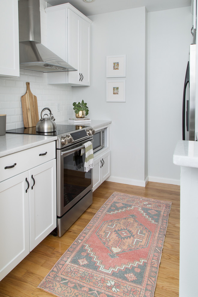 Zweizeilige, Kleine Klassische Küche mit Schrankfronten im Shaker-Stil, weißen Schränken, Rückwand aus Metrofliesen, Küchengeräten aus Edelstahl, braunem Holzboden und Küchenrückwand in Weiß in Boston