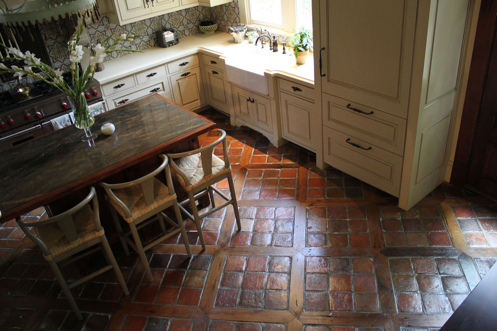 Inredning av ett medelhavsstil avskilt, mellanstort l-kök, med en rustik diskho, luckor med upphöjd panel, skåp i slitet trä, marmorbänkskiva, stänkskydd i keramik, klinkergolv i terrakotta och en köksö