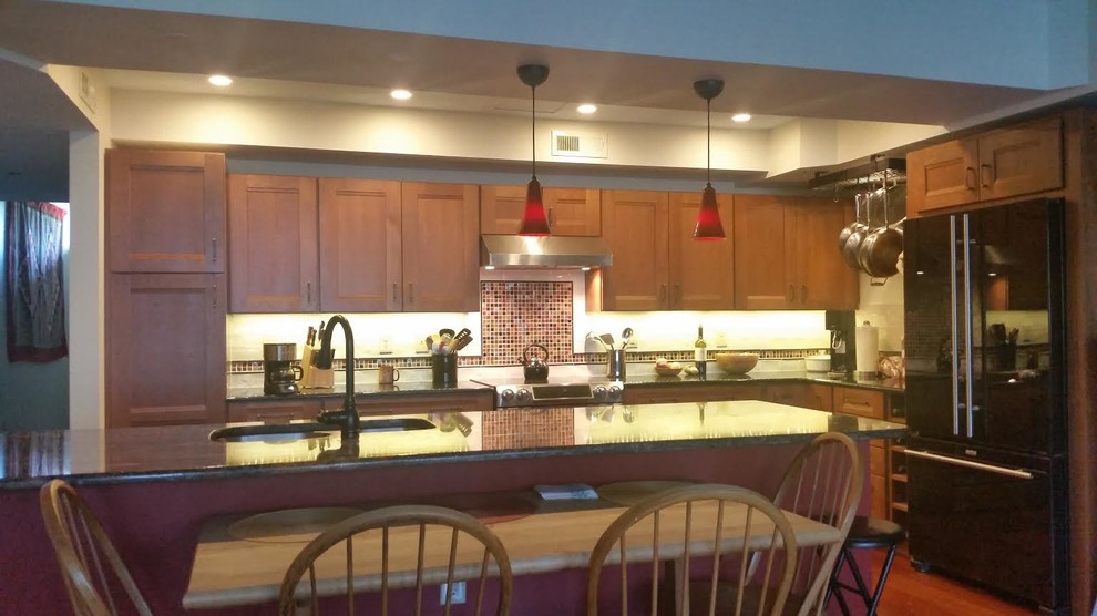Bild på ett mellanstort funkis kök, med skåp i mellenmörkt trä, brunt stänkskydd, stänkskydd i glaskakel, svarta vitvaror, mellanmörkt trägolv och en köksö