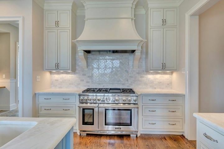 This is an example of a large classic u-shaped enclosed kitchen in Other with white cabinets, marble worktops, stainless steel appliances, a belfast sink, recessed-panel cabinets, white splashback, stone tiled splashback, medium hardwood flooring, an island and brown floors.