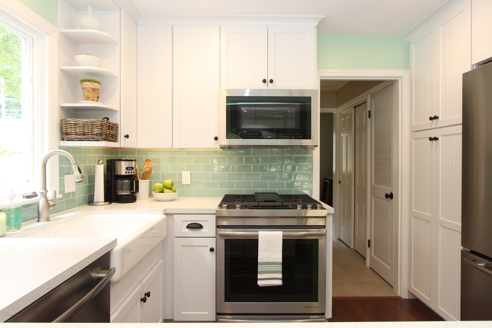 Klassisk inredning av ett avskilt, mellanstort u-kök, med en undermonterad diskho, luckor med profilerade fronter, vita skåp, laminatbänkskiva, grönt stänkskydd, stänkskydd i glaskakel, rostfria vitvaror, mellanmörkt trägolv och en halv köksö