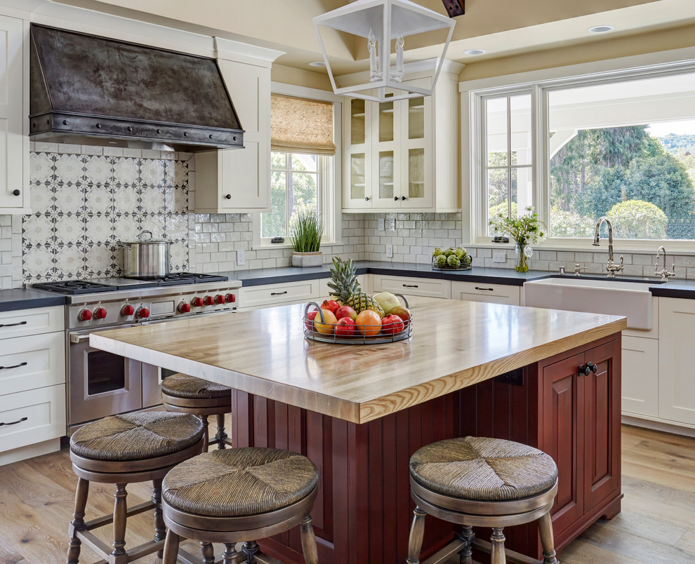 Bild på ett mellanstort lantligt grå grått kök, med en rustik diskho, skåp i shakerstil, vita skåp, bänkskiva i kvarts, vitt stänkskydd, stänkskydd i tunnelbanekakel, rostfria vitvaror, ljust trägolv, en köksö och flerfärgat golv