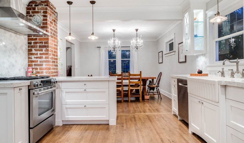 Eat-in kitchen - mid-sized traditional galley medium tone wood floor eat-in kitchen idea in Vancouver with a farmhouse sink, shaker cabinets, white cabinets, quartz countertops, gray backsplash, stone tile backsplash, stainless steel appliances and a peninsula