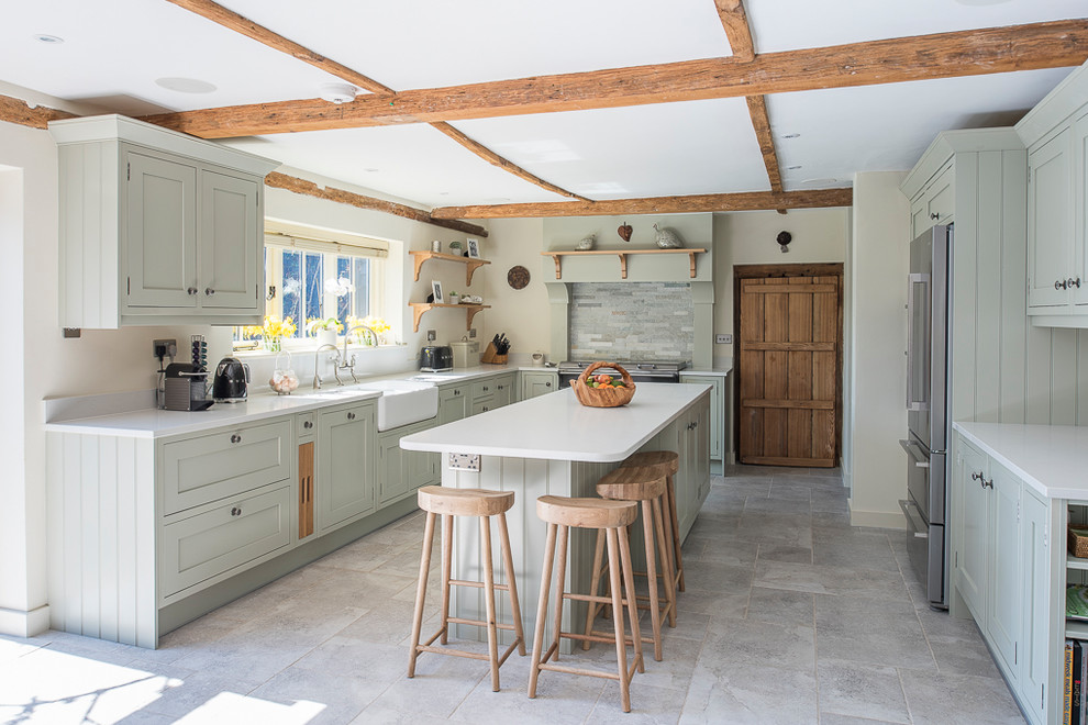 This is an example of a medium sized farmhouse l-shaped kitchen in Kent with a belfast sink, recessed-panel cabinets, green cabinets, quartz worktops, grey splashback, stainless steel appliances, an island, grey floors and white worktops.