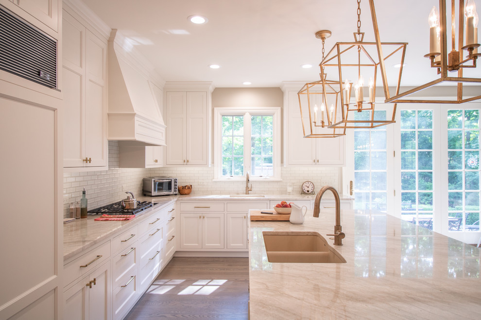 Large transitional l-shaped medium tone wood floor and brown floor open concept kitchen photo in Chicago with recessed-panel cabinets, white cabinets, white backsplash, subway tile backsplash, paneled appliances, an island and white countertops