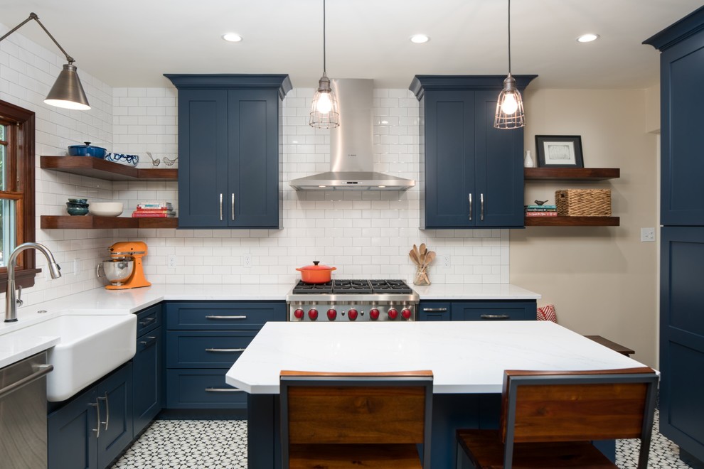 Small eclectic l-shaped kitchen/diner in Seattle with a belfast sink, raised-panel cabinets, blue cabinets, quartz worktops, white splashback, ceramic splashback, stainless steel appliances, cement flooring, an island and black floors.
