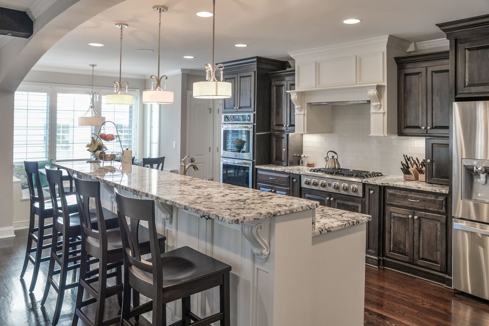 Inspiration for a mid-sized timeless single-wall dark wood floor and brown floor open concept kitchen remodel in Charlotte with raised-panel cabinets, dark wood cabinets, granite countertops, white backsplash, subway tile backsplash, stainless steel appliances, an island and beige countertops