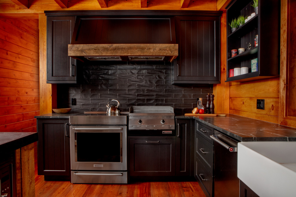 Idéer för mellanstora rustika svart kök, med en rustik diskho, skåp i shakerstil, svarta skåp, bänkskiva i kvarts, svart stänkskydd, rostfria vitvaror, mellanmörkt trägolv, en köksö och brunt golv