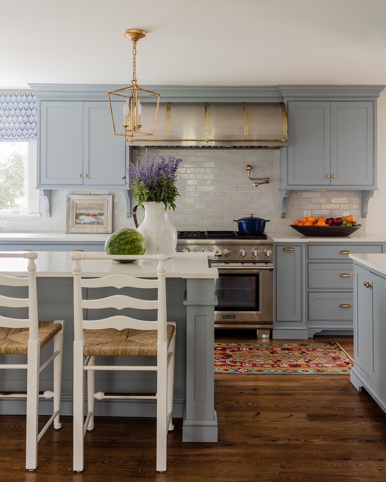 Bild på ett vintage kök, med luckor med profilerade fronter, blå skåp, grått stänkskydd, stänkskydd i tunnelbanekakel, rostfria vitvaror, mörkt trägolv och en köksö
