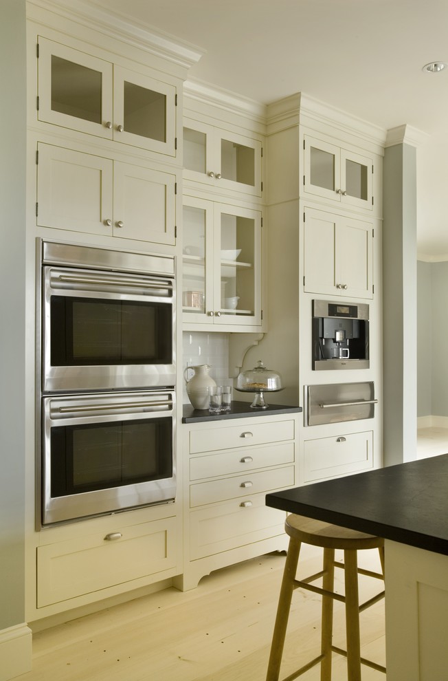 Bild på ett funkis kök, med skåp i shakerstil, rostfria vitvaror, stänkskydd i tunnelbanekakel, vita skåp och vitt stänkskydd