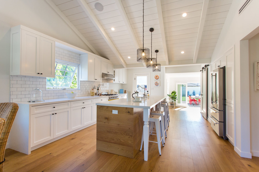 Example of a mid-sized country galley kitchen design in Los Angeles with a farmhouse sink, white cabinets, quartz countertops, white backsplash and stainless steel appliances