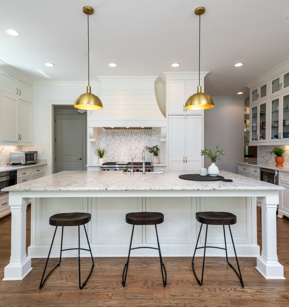 Photo of a large classic u-shaped kitchen/diner in Los Angeles with shaker cabinets, white cabinets, multi-coloured splashback, stainless steel appliances, medium hardwood flooring, an island, a belfast sink, granite worktops, marble splashback, brown floors and white worktops.