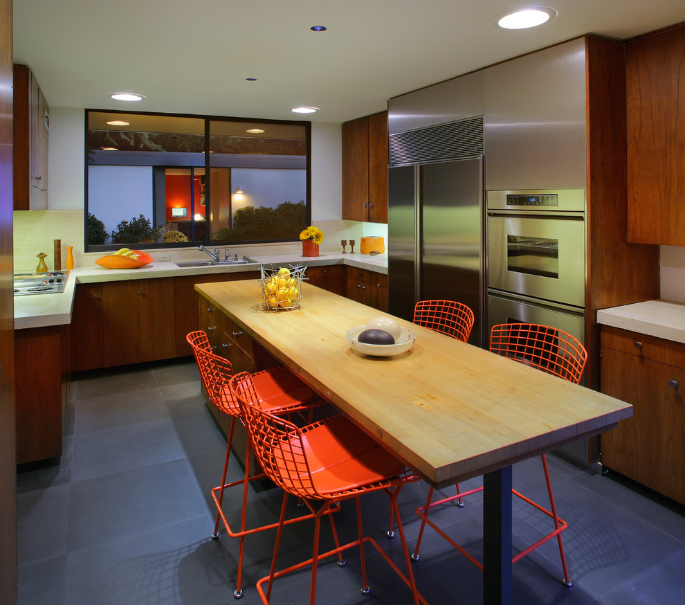Стильный дизайн: п-образная кухня среднего размера в стиле ретро с обеденным столом, накладной мойкой, плоскими фасадами, фасадами цвета дерева среднего тона, техникой из нержавеющей стали, островом и серым полом - последний тренд