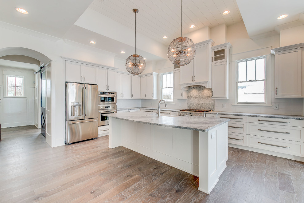 Eat-in kitchen - large craftsman l-shaped light wood floor and brown floor eat-in kitchen idea in Indianapolis with a farmhouse sink, shaker cabinets, white cabinets, quartzite countertops, blue backsplash, ceramic backsplash, stainless steel appliances and an island
