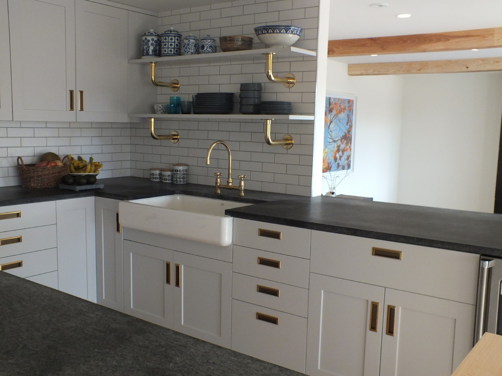 This is an example of a large scandinavian u-shaped open plan kitchen in Boston with a belfast sink, shaker cabinets, white cabinets, soapstone worktops, white splashback, metro tiled splashback, stainless steel appliances, light hardwood flooring and an island.