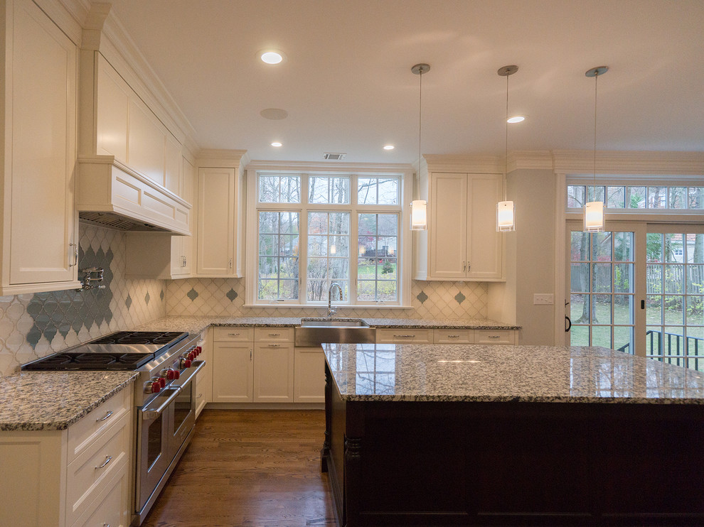 Inspiration for a large timeless medium tone wood floor kitchen remodel in New York with a drop-in sink, recessed-panel cabinets, white cabinets, granite countertops, white backsplash, stainless steel appliances and an island