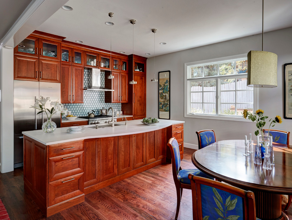 Eat-in kitchen - mid-sized contemporary galley medium tone wood floor eat-in kitchen idea in Denver with a single-bowl sink, shaker cabinets, medium tone wood cabinets, solid surface countertops, multicolored backsplash, ceramic backsplash, stainless steel appliances and an island