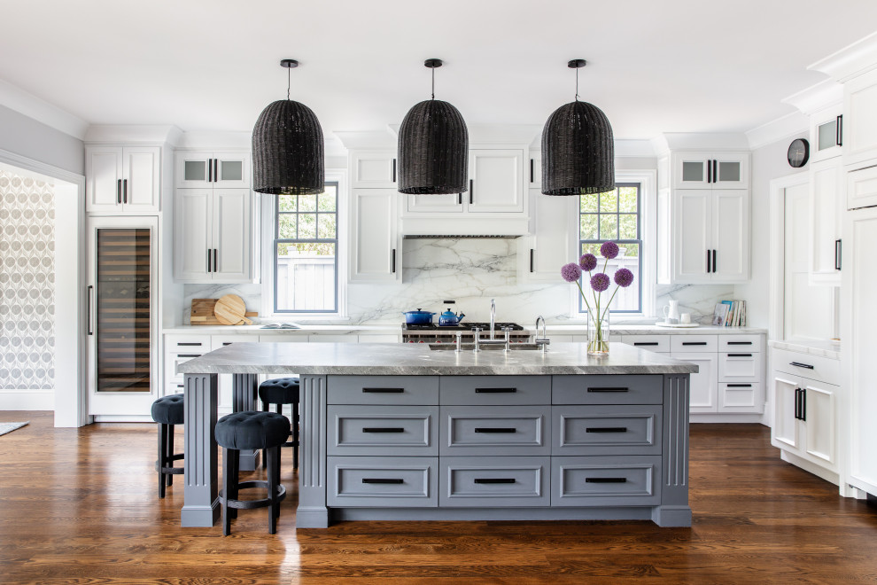 Foto på ett vintage grå l-kök, med en undermonterad diskho, vita skåp, vitt stänkskydd, stänkskydd i sten, integrerade vitvaror, mellanmörkt trägolv, en köksö, brunt golv och luckor med infälld panel