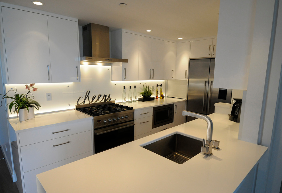 Photo of a medium sized modern galley kitchen in Vancouver with a submerged sink, flat-panel cabinets, white cabinets, white splashback, no island, brown floors, composite countertops, glass sheet splashback, stainless steel appliances and dark hardwood flooring.