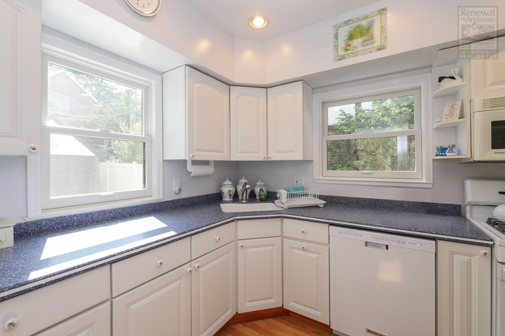 Immagine di una cucina a L chiusa e di medie dimensioni con lavello da incasso, ante bianche, paraspruzzi blu, elettrodomestici bianchi, pavimento in legno massello medio, pavimento marrone e top blu