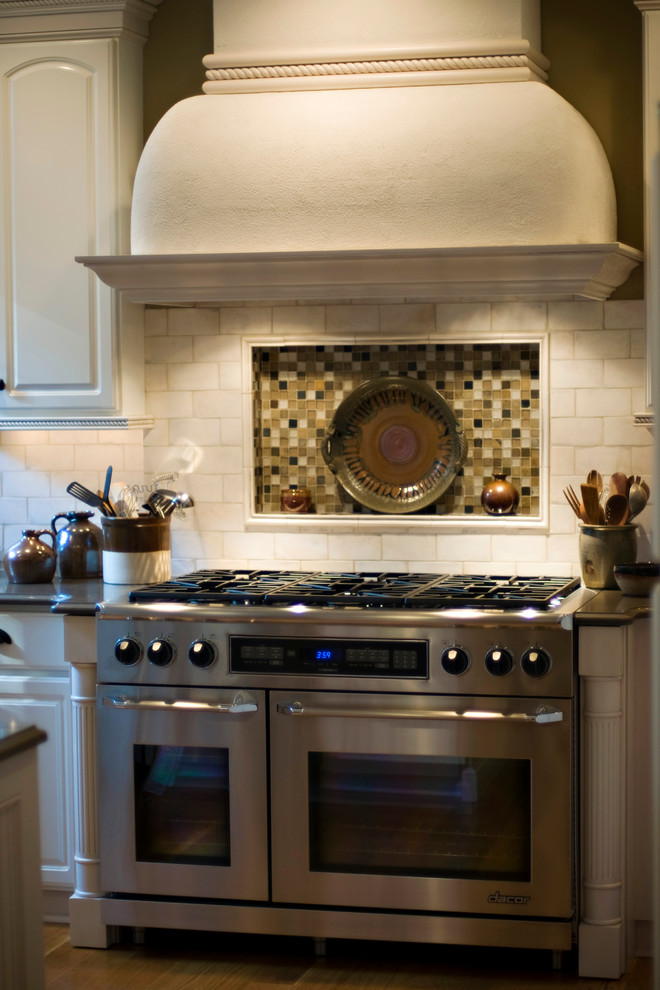 Modelo de cocina de estilo de casa de campo con fregadero bajoencimera, puertas de armario blancas, encimera de granito, salpicadero blanco, salpicadero de azulejos tipo metro, electrodomésticos de acero inoxidable, suelo de madera en tonos medios y una isla