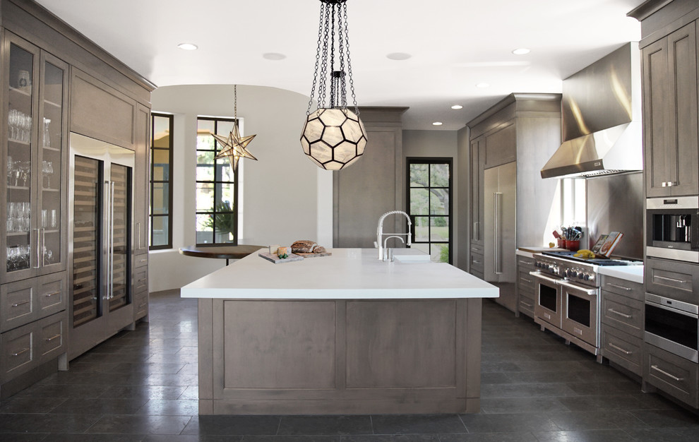 Inspiration for a huge transitional galley limestone floor and black floor eat-in kitchen remodel in Phoenix with metallic backsplash, stainless steel appliances, an island, a farmhouse sink, glass-front cabinets, marble countertops, marble backsplash, white countertops and gray cabinets