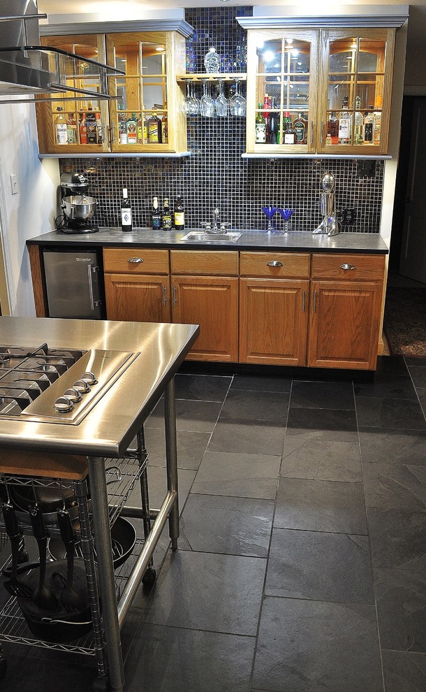 Eklektisk inredning av ett mellanstort kök, med en nedsänkt diskho, luckor med upphöjd panel, skåp i mellenmörkt trä, bänkskiva i rostfritt stål, svart stänkskydd, stänkskydd i glaskakel, rostfria vitvaror, skiffergolv och en köksö