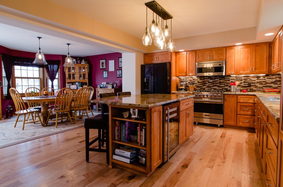 Example of a large classic l-shaped medium tone wood floor eat-in kitchen design in Other with a double-bowl sink, shaker cabinets, medium tone wood cabinets, granite countertops, multicolored backsplash, glass tile backsplash, stainless steel appliances and an island