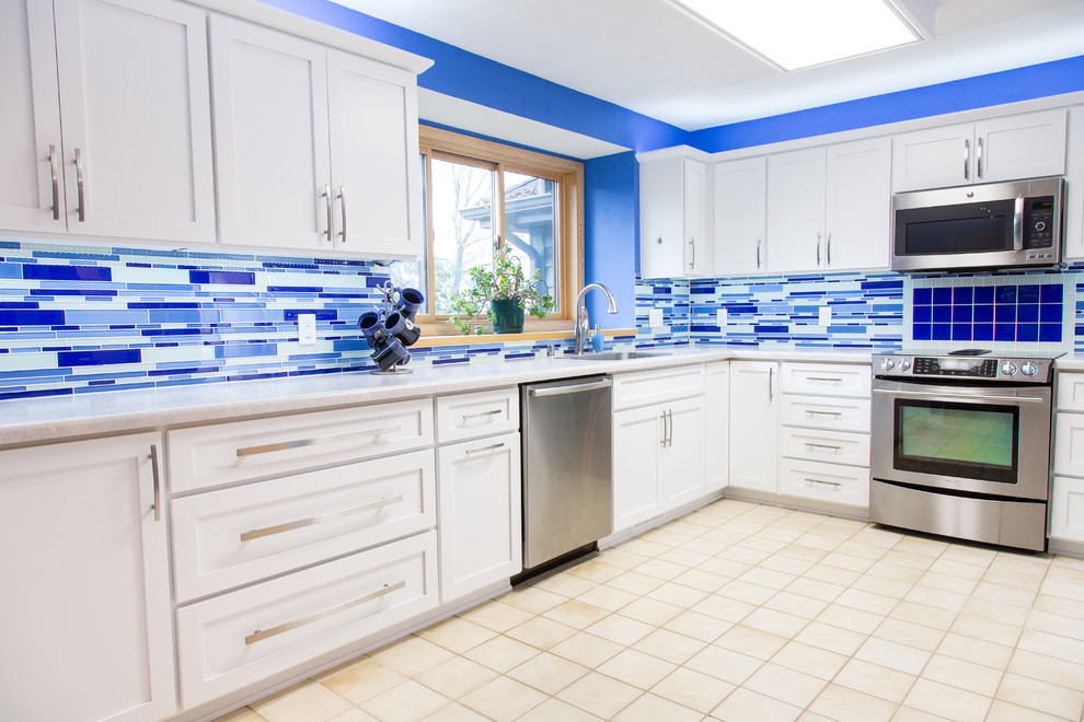 他の地域にあるお手頃価格の中くらいなコンテンポラリースタイルのおしゃれなキッチン (アンダーカウンターシンク、白いキャビネット、ラミネートカウンター、青いキッチンパネル、シルバーの調理設備、フラットパネル扉のキャビネット、ガラスタイルのキッチンパネル、セラミックタイルの床、アイランドなし、ベージュの床、白いキッチンカウンター) の写真
