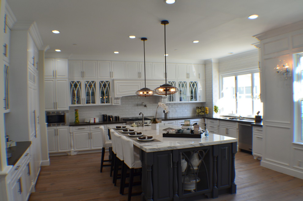 Example of a large classic u-shaped light wood floor and brown floor eat-in kitchen design in Los Angeles with an undermount sink, raised-panel cabinets, quartz countertops, white backsplash, ceramic backsplash, stainless steel appliances, an island, white cabinets and white countertops