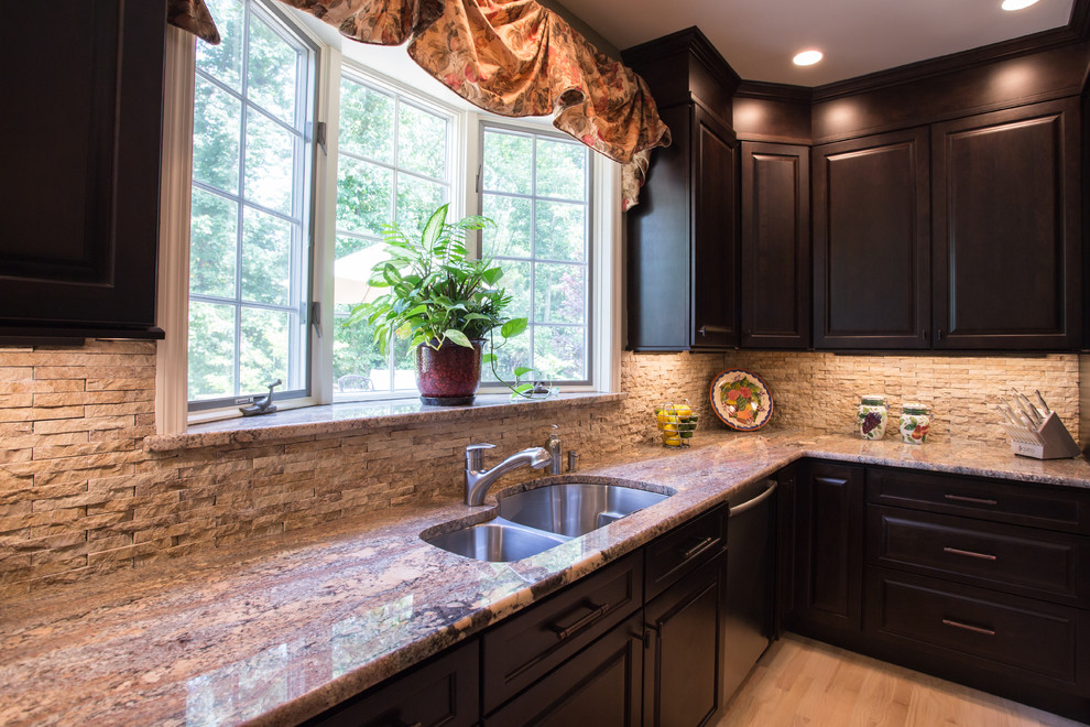 Example of a large tuscan u-shaped light wood floor eat-in kitchen design in New York with raised-panel cabinets, dark wood cabinets, granite countertops, beige backsplash, stone tile backsplash, stainless steel appliances, an island and a double-bowl sink