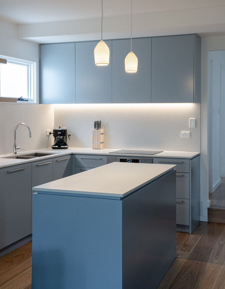 Idéer för att renovera ett mellanstort minimalistiskt vit vitt kök, med en undermonterad diskho, släta luckor, blå skåp, bänkskiva i kvarts, vitt stänkskydd, rostfria vitvaror, mellanmörkt trägolv, en köksö och brunt golv